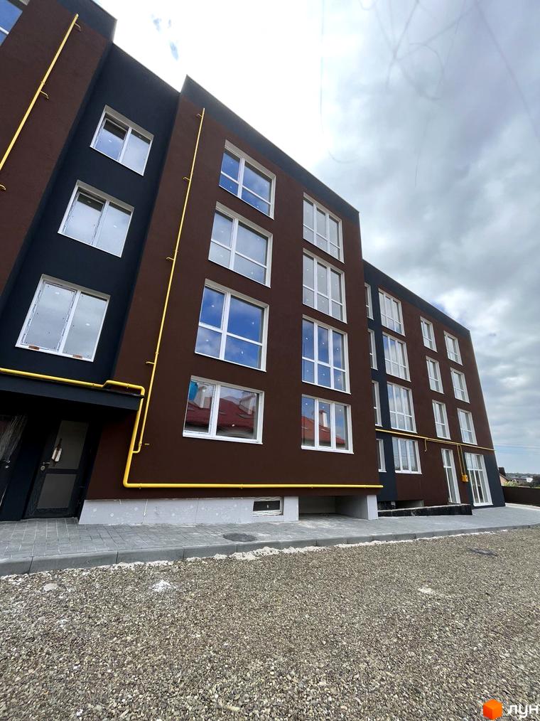 Зовнішній вигляд багатоповерхового будинку ЖК Зубра Дім з коричневим фасадом та великими вікнами, поруч з будинком прибудинкова територія з гравієм.