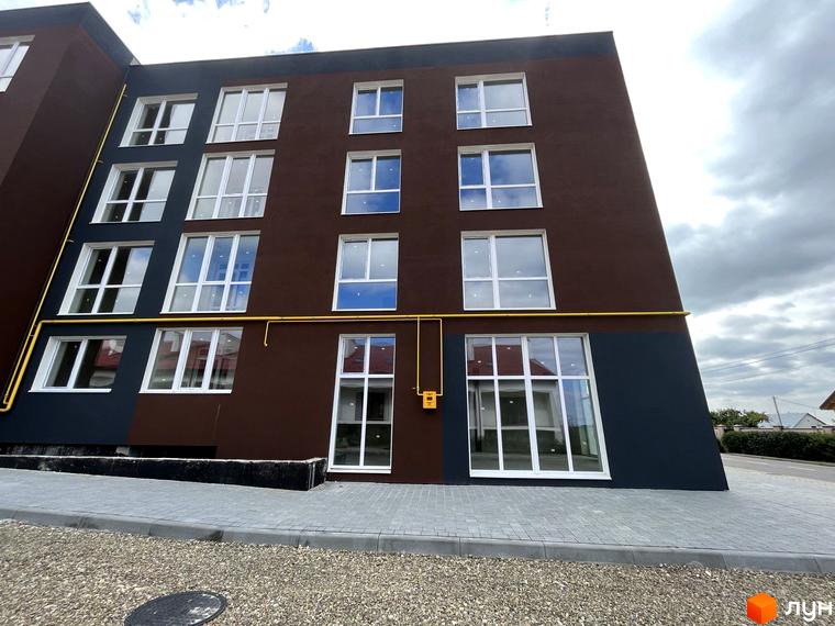 Фасад багатоповерхового будинку ЖК Зубра Дім з великими вікнами та газовою трубою. Біля будинку тротуар з бруківки та гравій.