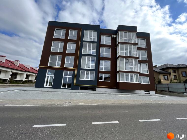 Багатоповерховий будинок ЖК Зубра Дім з панорамними вікнами на тлі неба. На передньому плані асфальтована дорога та тротуар.