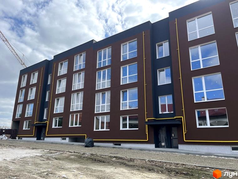 Зовнішній вигляд новобудови ЖК Зубра Дім з коричневим фасадом та численними вікнами на тлі хмарного неба. На передньому плані видно будівельний майданчик.