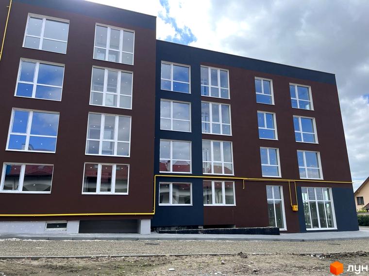 Зовнішній вигляд багатоповерхового будинку ЖК Зубра Дім з великими вікнами. На передньому плані видно прибудинкову територію з гравієм.