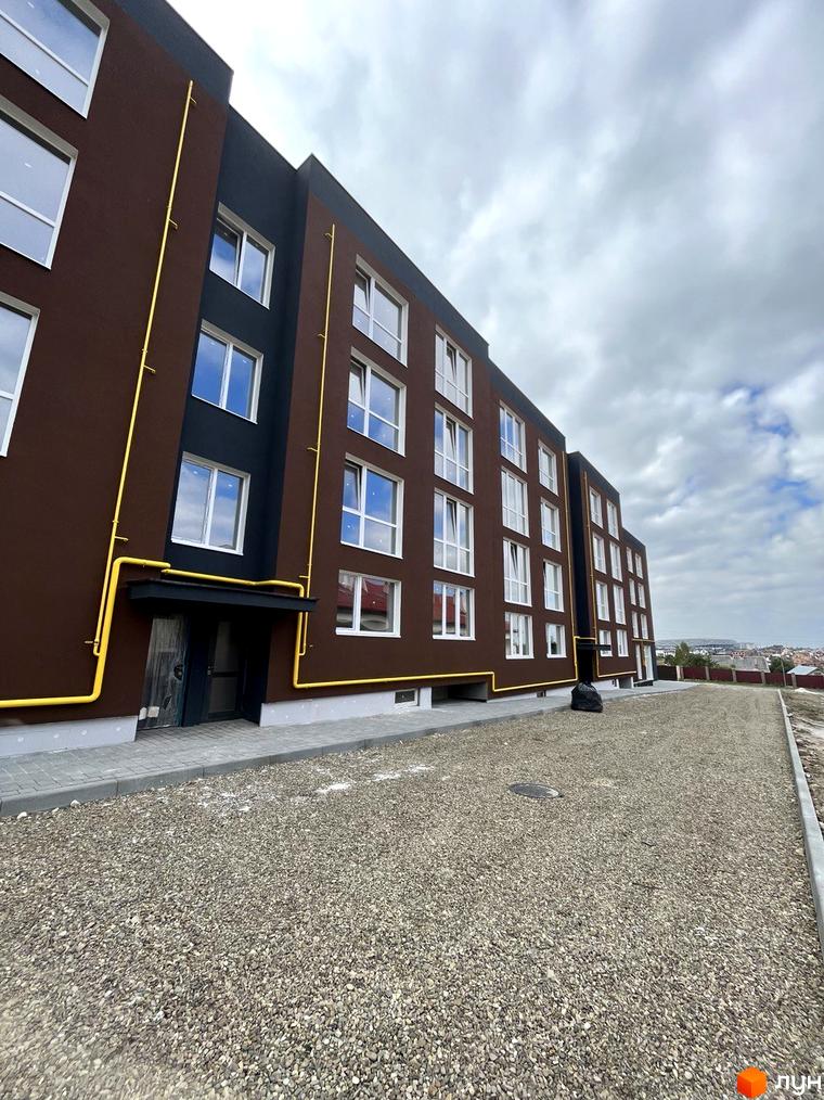 Зовнішній вигляд будинку ЖК Зубра Дім з коричневим фасадом та жовтими трубами. Поруч розташована прибудинкова територія з гравієм.