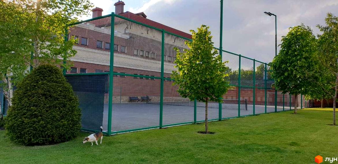 Зовнішній вигляд Котеджного містечка Аріадна з зеленим парканом та сіткою. На території ростуть дерева та кущі, є газон.