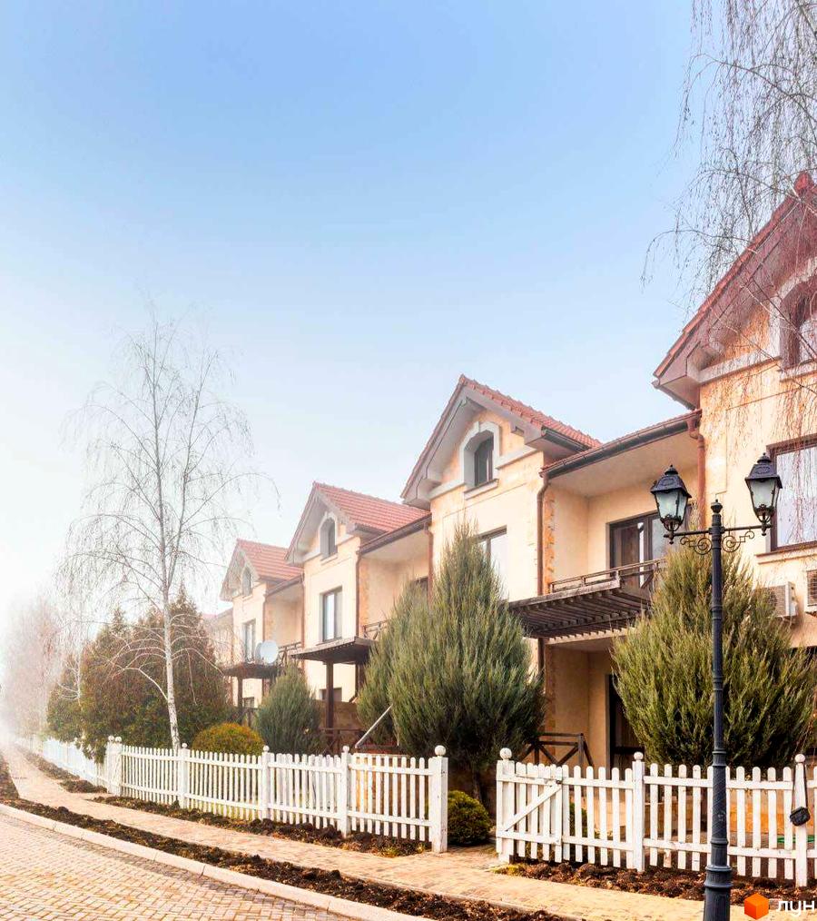 Зображення котеджів у Містечку котеджів Аріадна з черепичними дахами та білими парканами. Вигляд на прибудинкову територію з деревами.