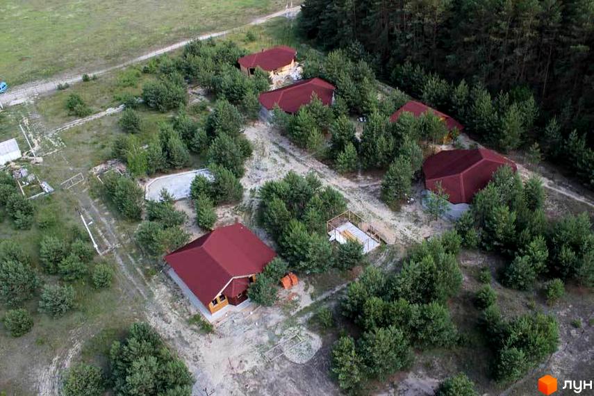 Фото Котеджне містечко Дачне село. Будинки з червоними дахами серед зелених дерев. Навколо котеджів піщаний ґрунт.