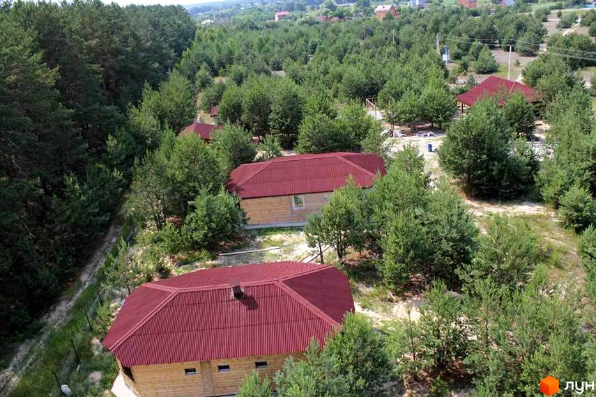 Зовнішній вигляд котеджного комплексу КМ Дачне село з червоними дахами серед зелених насаджень. Прибудинкова територія з доріжками та деревами.