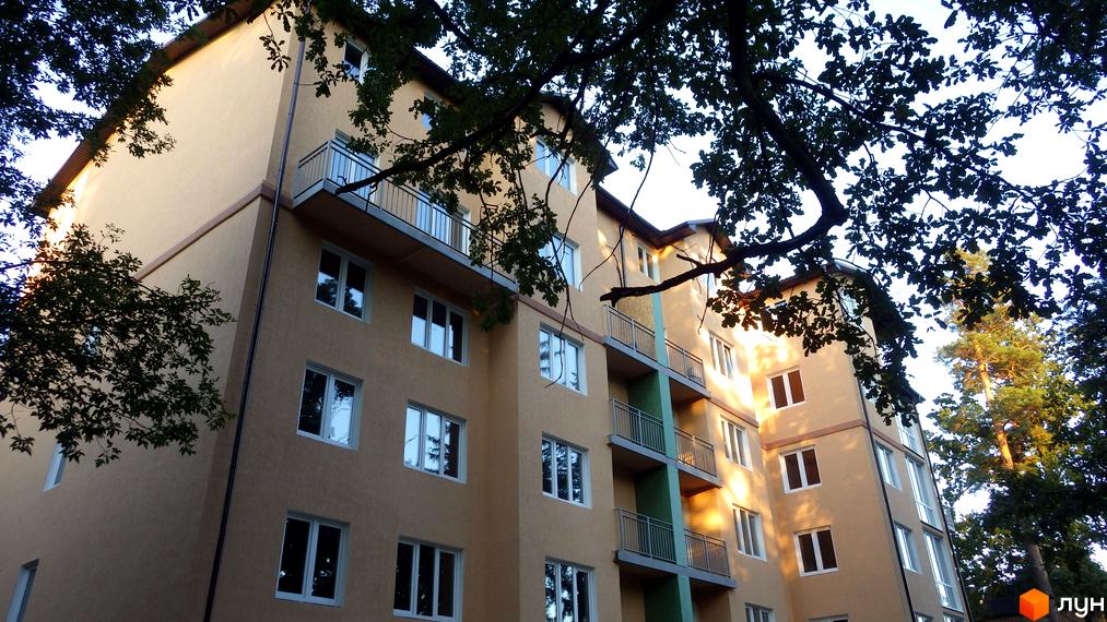 Житловий комплекс Курортний. Фасад будівлі кремового кольору з балконами та вікнами. Навколо будівлі ростуть дерева.