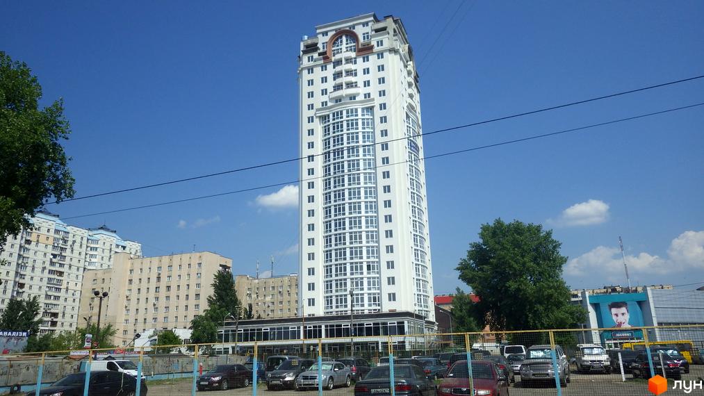 Зображення Житлового комплексу Оболонь Тауер. Високий білий будинок з великою кількістю вікон на фоні блакитного неба.