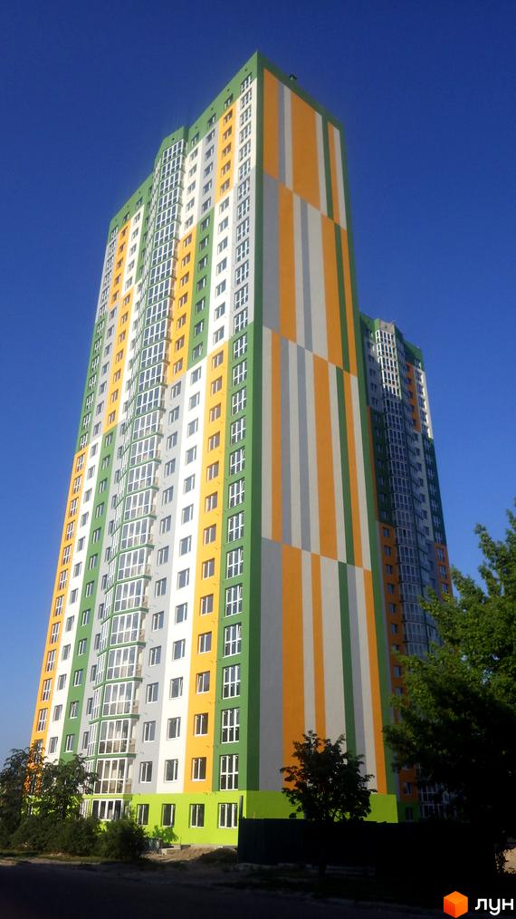 Яскрава новобудова на вул. Петра Калнишевського (Майорова), 6 з фасадом у смужку зеленого, жовтого та сірого кольорів. Перед будинком розташовані дерева та зелені насадження.