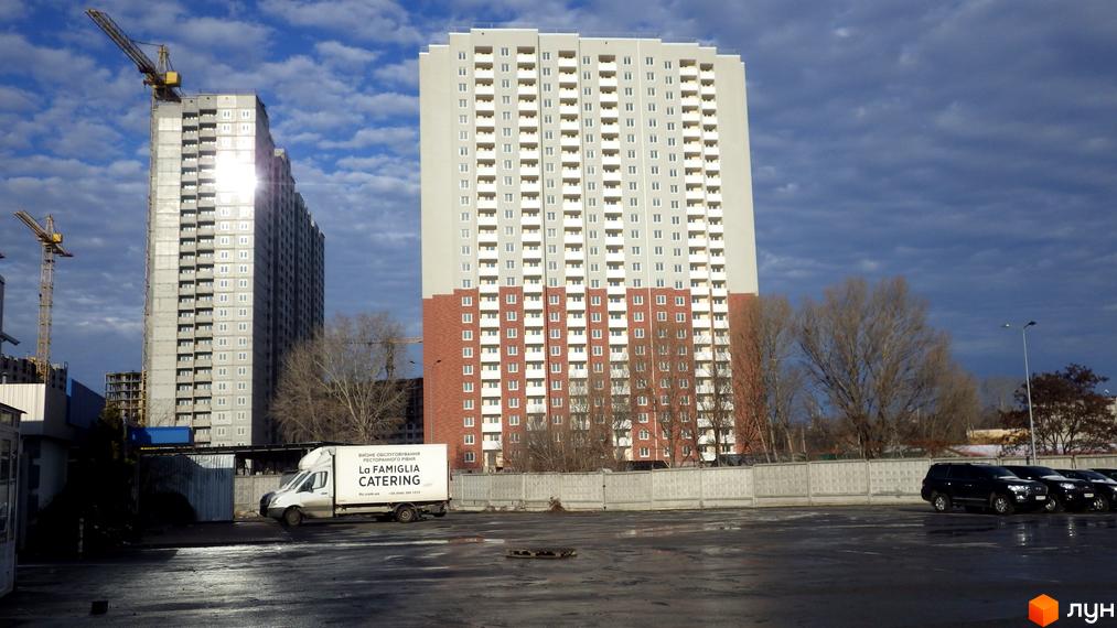 Житловий комплекс Navigator: висотна будівля зі світло-сірим та цегляним фасадом, поруч інша у процесі будівництва. На передньому плані парковка.