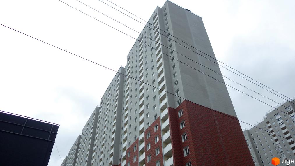 Новобудова Navigator: високий багатоквартирний будинок з сірим фасадом та червоною цегляною обробкою нижніх поверхів.