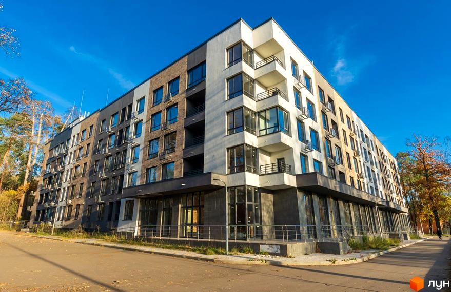 Багатоповерховий Апарт-комплекс в Пущі Водиці з фасадами різних кольорів та великими вікнами. Будівля розташована біля дороги, оточена деревами.