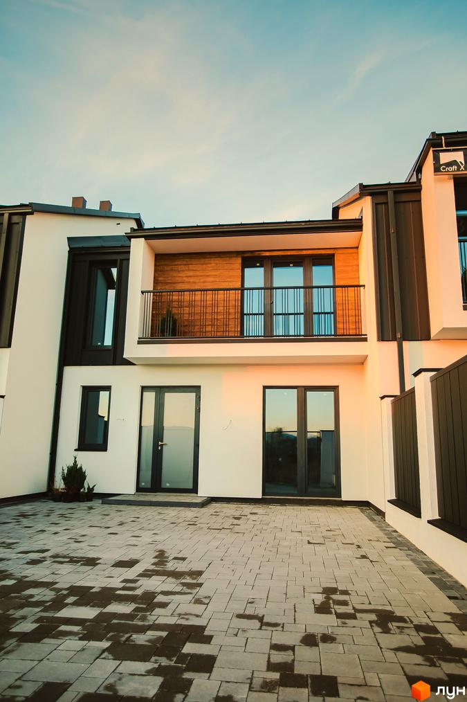 Таунхауси Modern House з білою фасадною частиною, дерев'яними елементами та балконом. Перед будинком вимощена сіра плитка з мокрими ділянками.