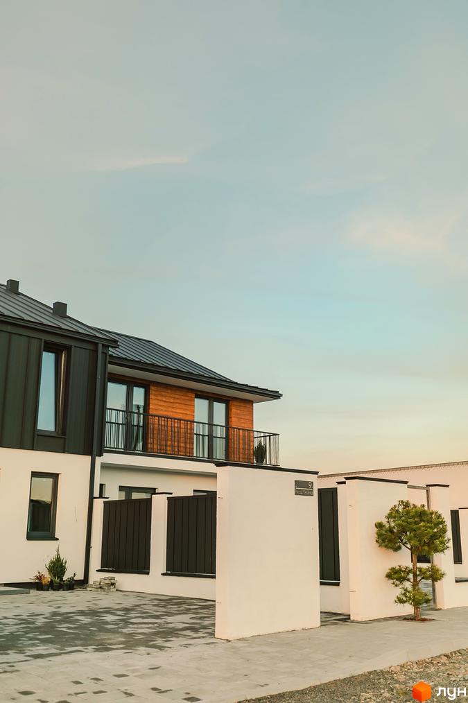 Таунхауси Modern House з білими стінами, темними дахами та дерев'яними елементами фасаду. Прибудинкова територія з бруківкою та зеленими насадженнями.