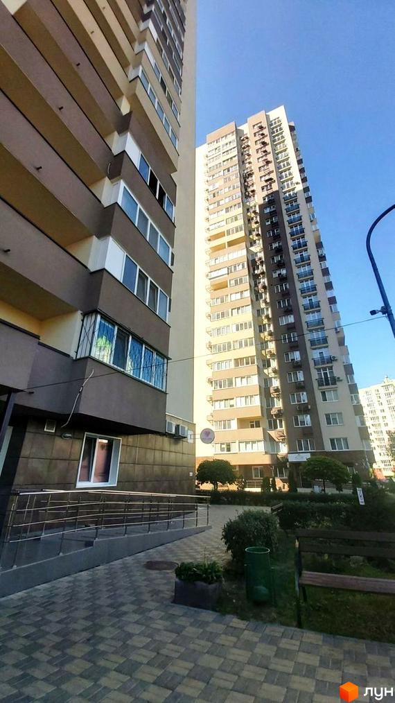 Зовнішній вигляд багатоповерхових будинків житлового комплексу Friendly House. Прибудинкова територія з зеленими насадженнями та лавками.