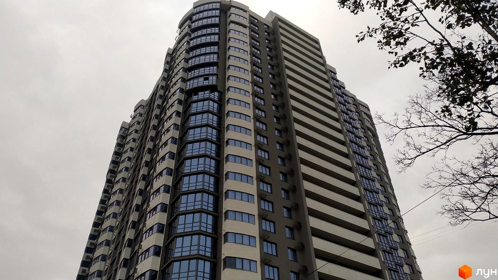 Висотна будівля ЖК FREEDOM з великою кількістю вікон. Сіре небо та гілки дерев на тлі.