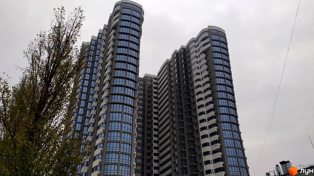 Багатоповерховий будинок ЖК FREEDOM з великою кількістю вікон на тлі сірого неба. Поруч з будинком росте дерево.