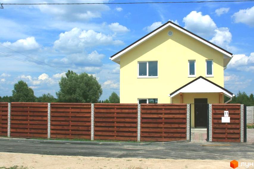 Фото будинку в Котеджному містечку Солнечная Поляна. Двоповерховий будинок жовтого кольору з коричневим дахом та дерев'яним парканом.