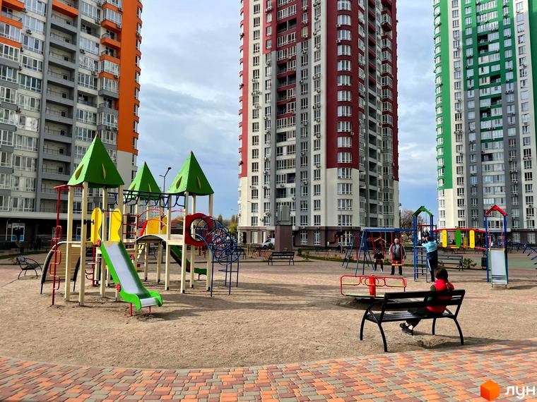 Житловий комплекс Каховська: багатоповерхові будинки з яскравими фасадами (червоний, зелений, помаранчевий) та дитячий майданчик із гірками та гойдалками.