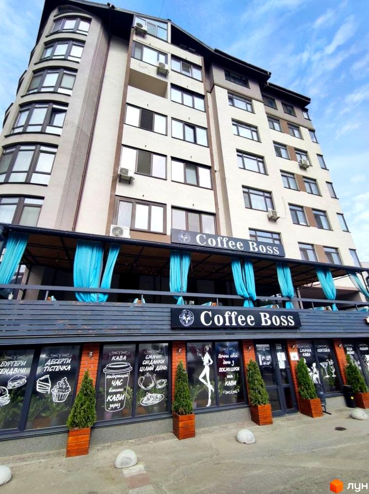 Багатоповерховий будинок ЖБ Light house світлого кольору з численними вікнами. На першому поверсі розташоване кафе Coffee Boss з вітринами та літнім майданчиком.