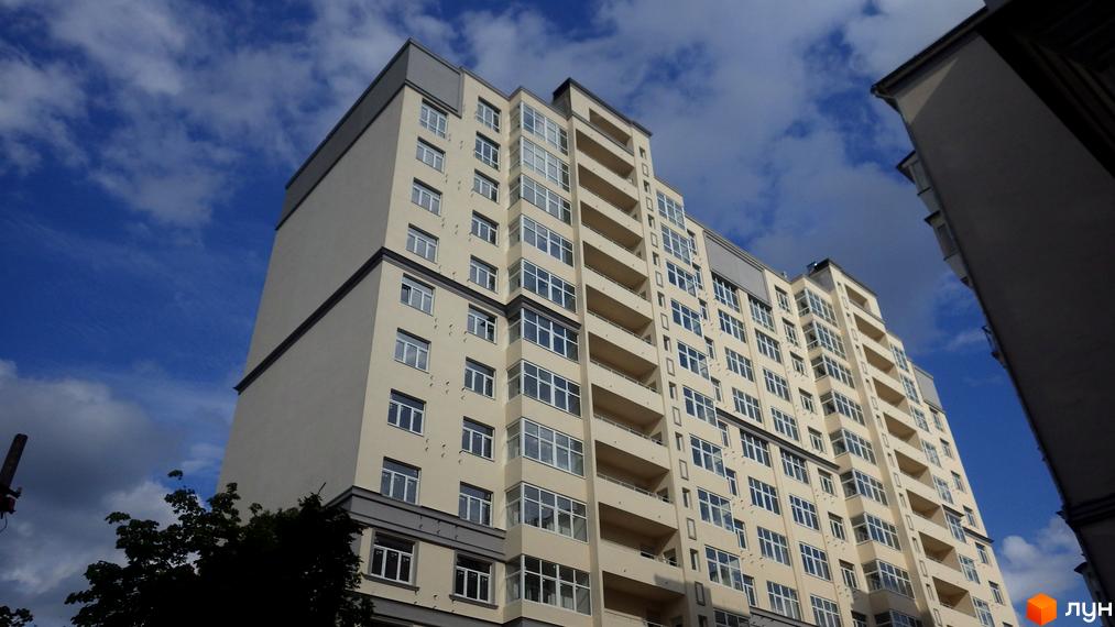 Житловий комплекс Дом на Строителей – це сучасна багатоповерхова новобудова з великою кількістю вікон та балконів. Будинок має світлий фасад та сірий дах, що гармонійно виглядає на фоні блакитного неба.