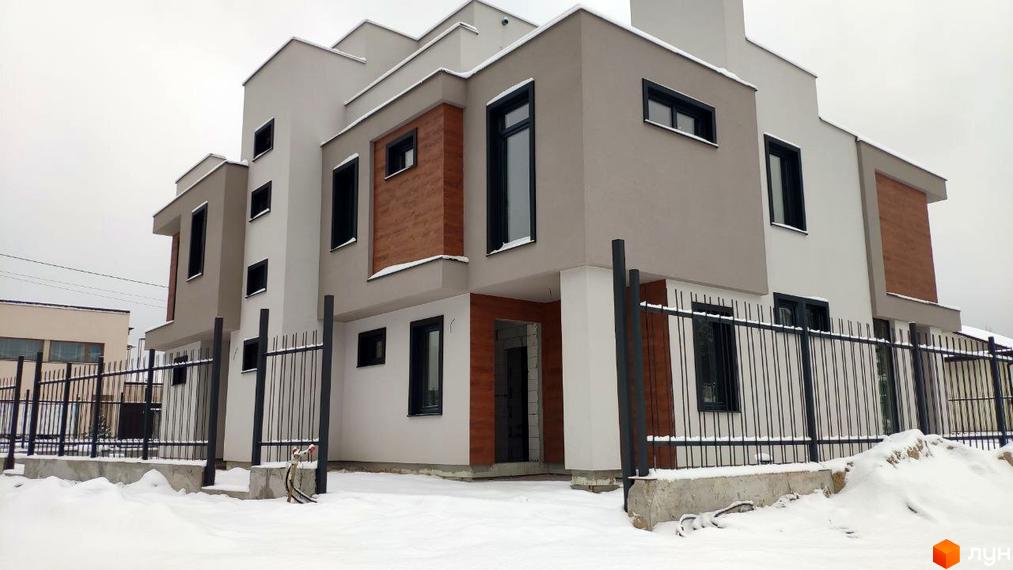 Зовнішній вигляд будинку житлового комплексу Дуплекси „Сосновий бір“: двоповерховий будинок з білими та коричневими стінами, чорними вікнами та огорожею, вкритий снігом.