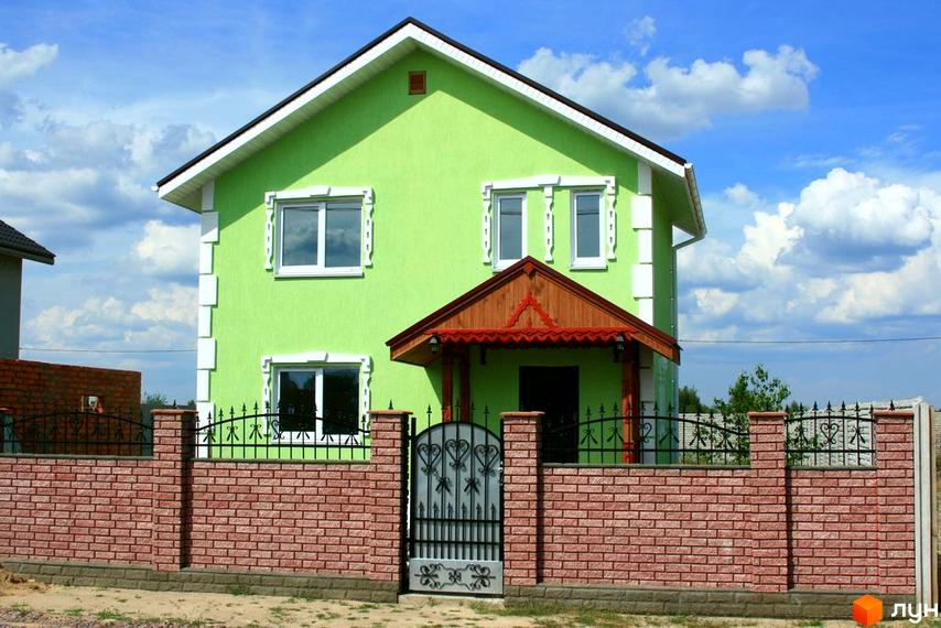 Будинок житлового комплексу КМ Солнечная Поляна з зеленим фасадом та дерев'яним навісом. Прибудинкова територія огороджена цегляним парканом.
