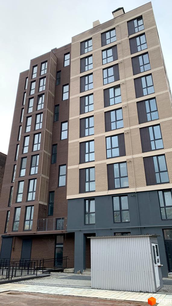 Висотна будівля Житлового комплексу з цегляними фасадами. На передньому плані - прибудинкова територія з бруківкою та металевою спорудою.