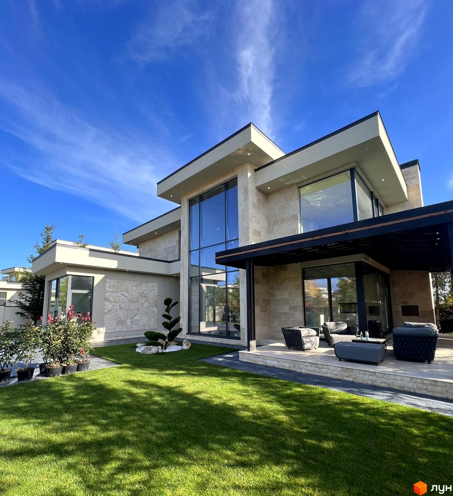 Вигляд котеджу в Котеджному містечку Riviera City Park. Світлий фасад будинку з великими вікнами та зелений газон перед ним.