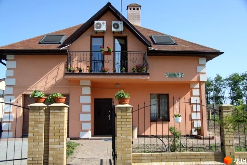 Фото будинку в Котеджному містечку Європа. Двоповерховий будинок з балконом, коричневим дахом, огорожею та зеленими насадженнями.