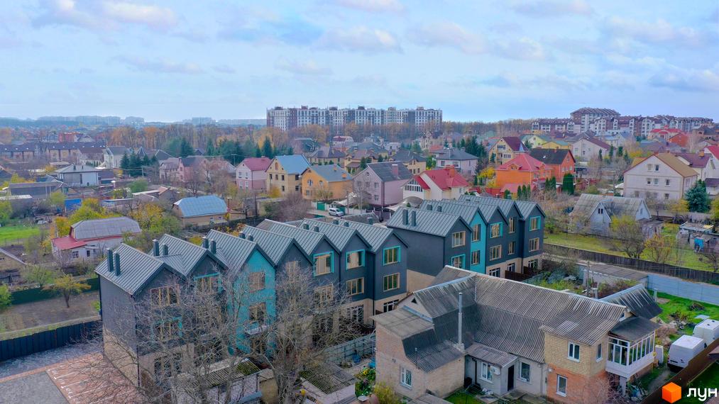 Таунхауси New Smart 13 - це комплекс з сучасними будинками та доглянутою прибудинковою територією. На зображенні видно фасади будинків та зелену зону навколо.