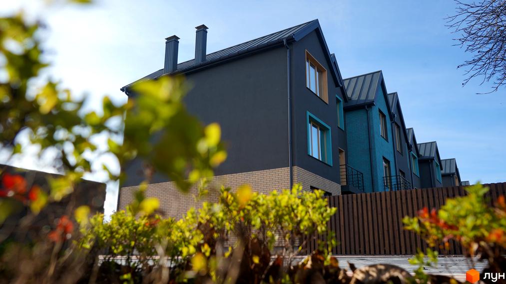 Зовнішній вигляд таунхаусів New Smart 13 з цегляною обробкою та темними фасадами, на тлі блакитного неба та зелені.