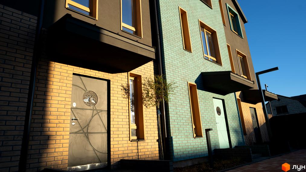 Таунхауси New Smart 13: фасади будинків з жовтої та бірюзової цегли, великі вікна та двері. Прибудинкова територія з бруківкою та освітленням.