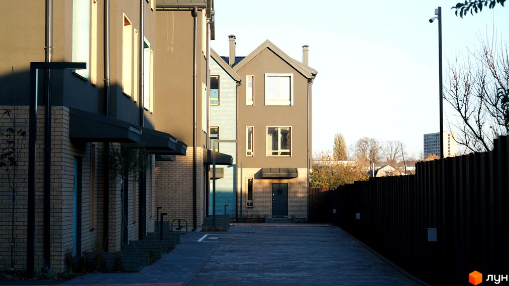 Таунхауси New Smart 13 з цегляними першими поверхами та сірими фасадами, огороджені парканом, з вимощеною доріжкою.