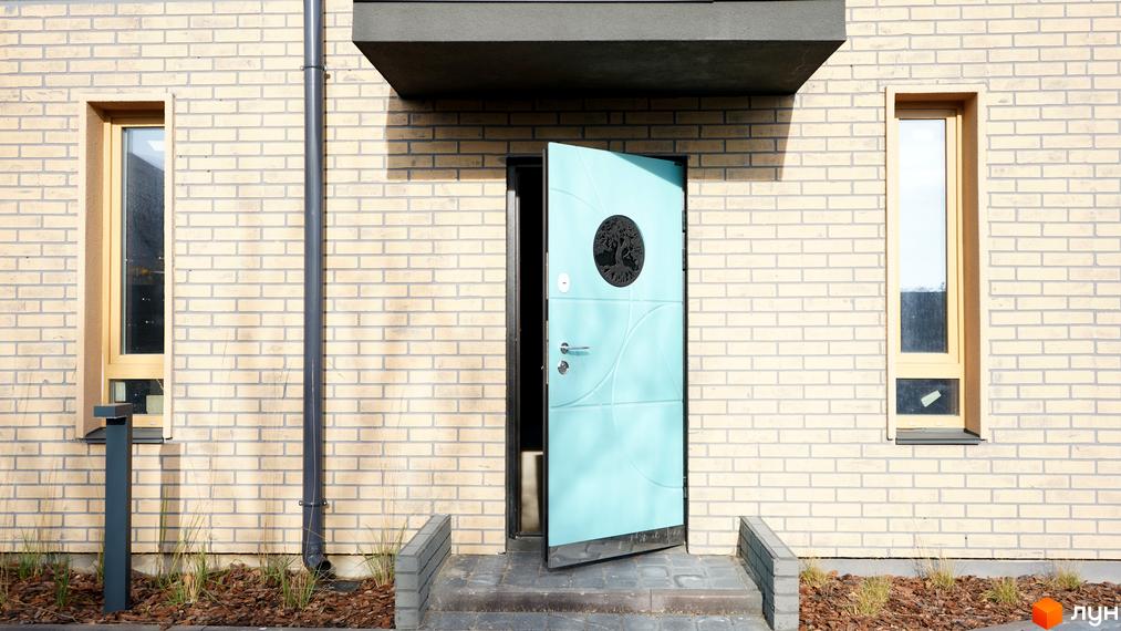 Фасад будинку таунхаусів New Smart 13 з білої цегли, блакитними дверима та вікнами. Біля будинку доріжка та зелені насадження.