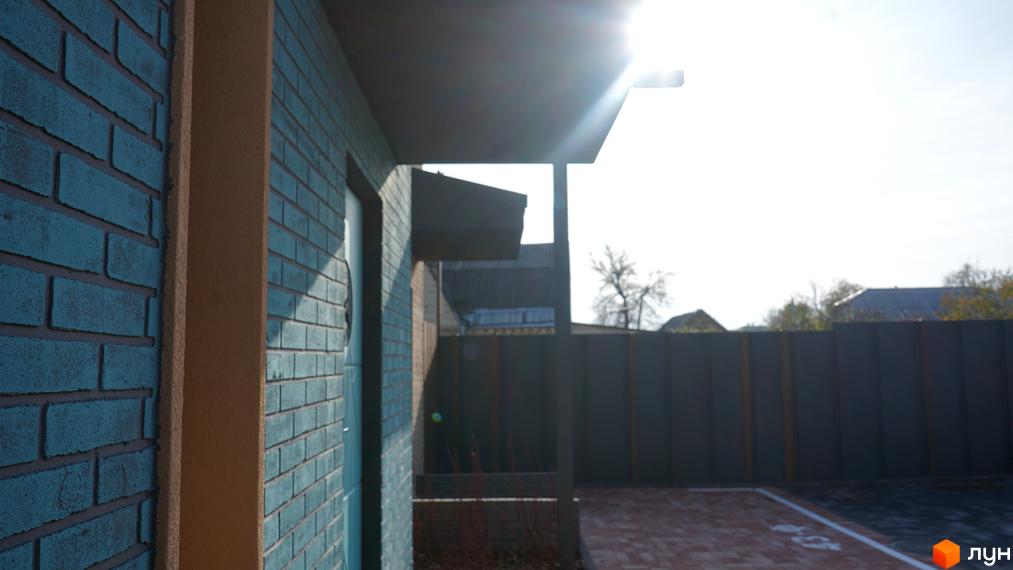 Зовнішній вигляд таунхаусів New Smart 13 з блакитної цегли та прибудинкова територія з бруківки та паркану.