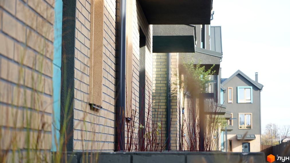 Фасад таунхаусів New Smart 13 з цегляним оздобленням та елементами сірого кольору. Навколо новобудови зелені насадження та паркан.