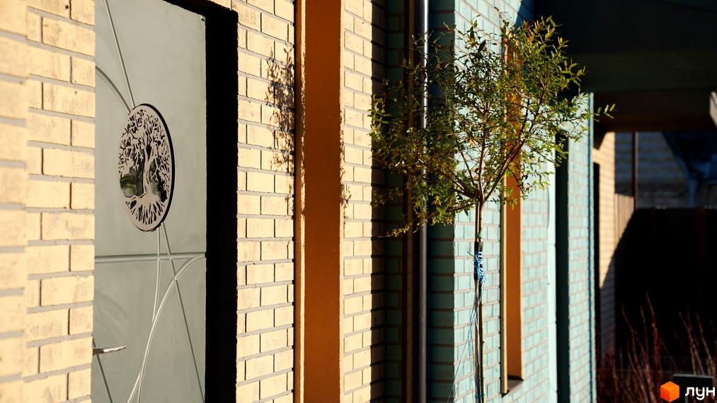 Таунхауси New Smart 13: фасад будинку з цегляним оздобленням та декоративним деревом біля входу. Прибудинкова територія з деревами та парканом.