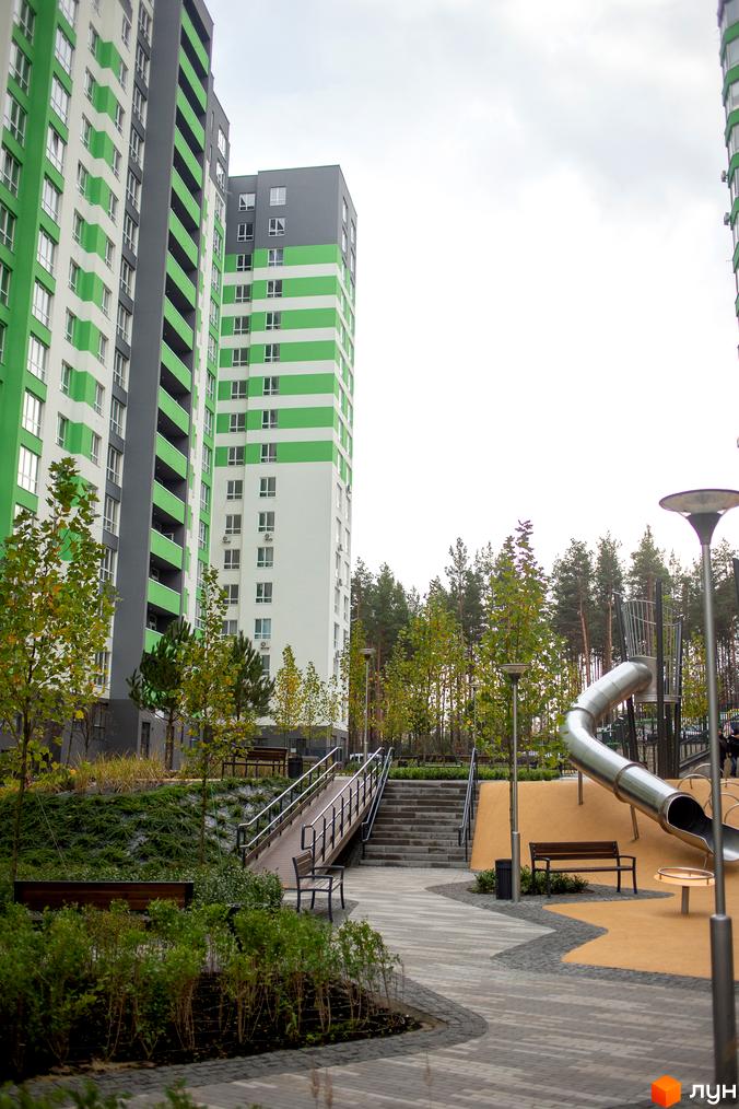 Новобудова ЖК City Park з яскравим фасадом та дитячим майданчиком із гіркою. Зелені насадження та лавочки створюють затишну атмосферу.
