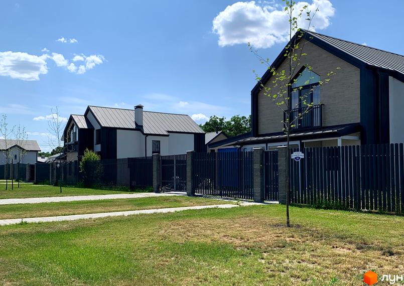Котеджне містечко КМ Зелений Бульвар. Зовнішній вигляд будинків з металевими дахами та парканом, зелена прибудинкова територія з газоном та деревами.