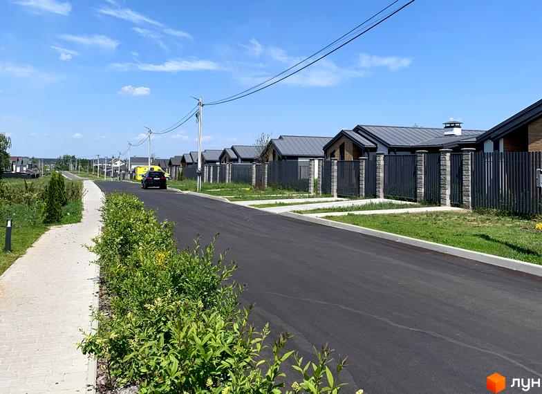 КМ Зелений Бульвар: котеджне містечко з сучасними будинками та доглянутою прибудинковою територією. Асфальтована дорога веде до будинків, вздовж якої висаджені зелені насадження.