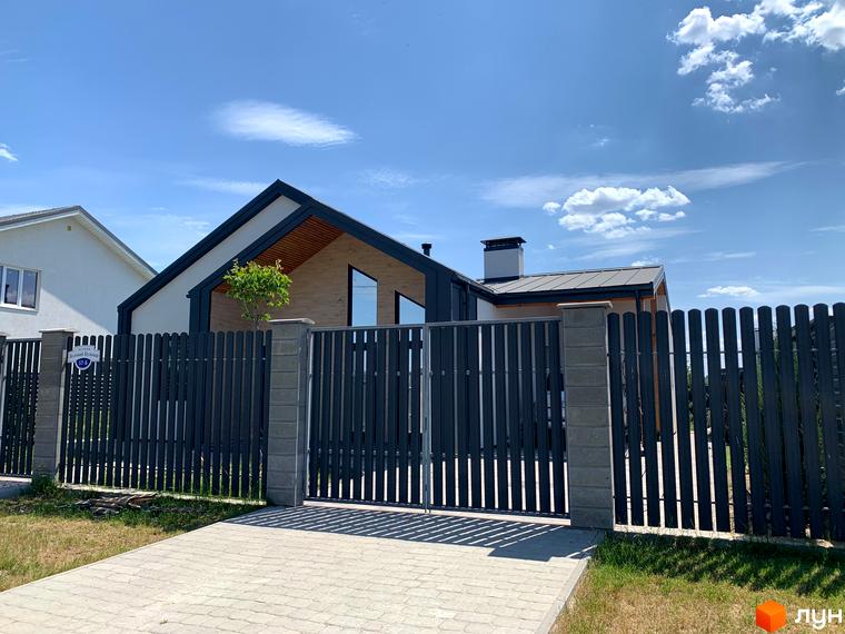 Котеджне містечко Зелений Бульвар. Зовнішній вигляд будинку з сірим парканом та воротами, вимощеною доріжкою та зеленою ділянкою під блакитним небом.