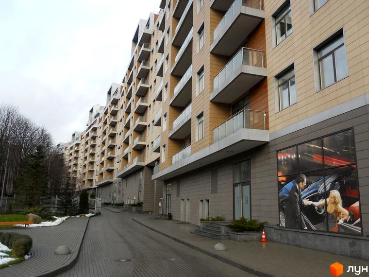 Зовнішній вигляд житлового комплексу Crystal Park з балконами та сучасним фасадом. Прибудинкова територія з зеленими насадженнями та пішохідною доріжкою.