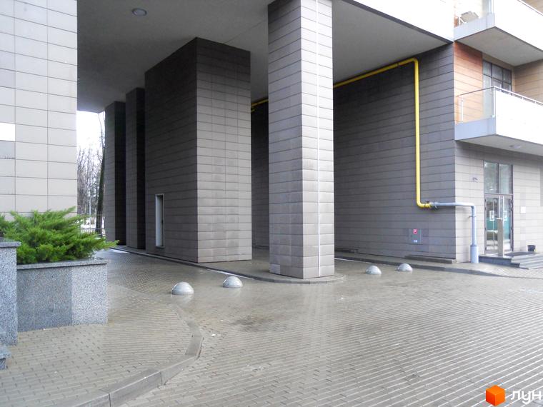 Вхідна група житлового комплексу Crystal Park з великими колонами та прибудинковою територією, викладеною плиткою.