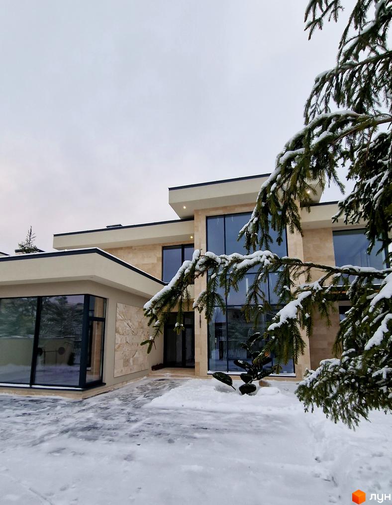 Зимовий пейзаж Котеджного містечка Riviera City Park з будинком з великими вікнами та засніженою прибудинковою територією.