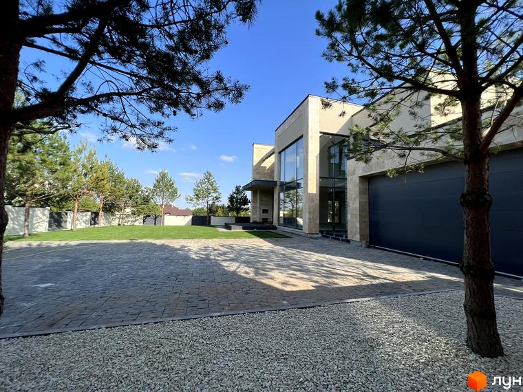 Котеджне містечко Riviera Royal. Фасад будинку з великими вікнами та гаражними воротами, прибудинкова територія з газоном та бруківкою.