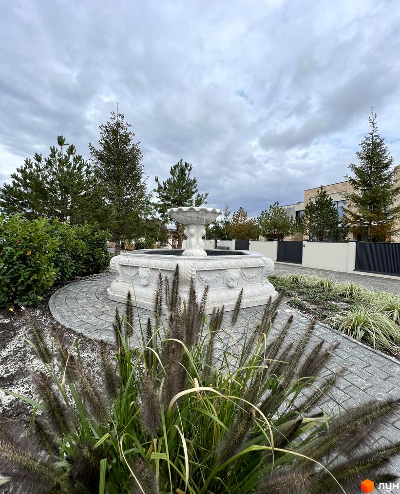 Котеджне містечко Riviera Royal: кам'яний фонтан та зелені насадження на фоні сучасних будинків.