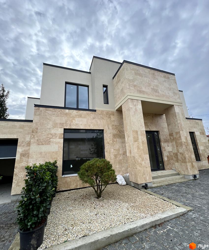 Котеджне містечко Riviera Royal: фасади будинку оздоблені світлим каменем, великі вікна, перед будинком зелені насадження та гравій.