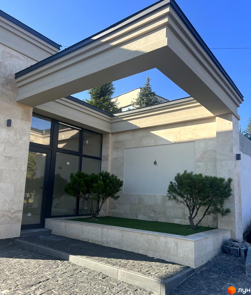 Зовнішній вигляд будинку КМ Riviera Royal з кам'яним оздобленням та великими вікнами, прибудинкова територія з газоном та декоративними деревами.