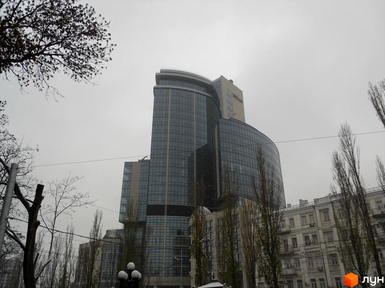 Житловий комплекс H-Tower з сучасним фасадом та великою скляною поверхнею, оточений зеленими насадженнями та прибудинковою територією.